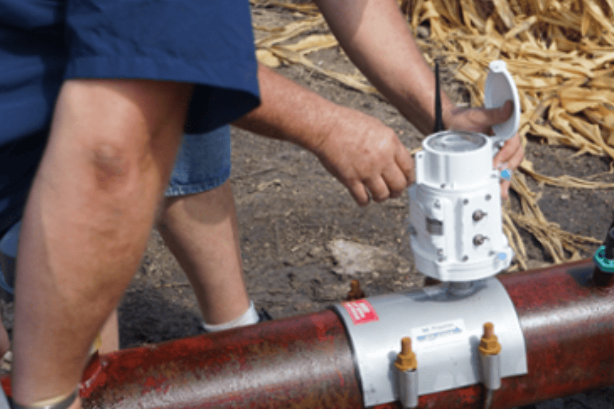 Outdoors image of a man bent over red pipeline and open telemetry unit.
