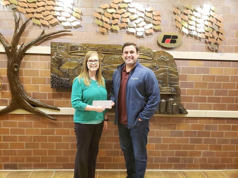 Megahn Schafer (left), Executive Director of the Nebraska Farm Bureau, receives donation check presented by Rob Collier (right), President of McCrometer, on April 18th, 2019.